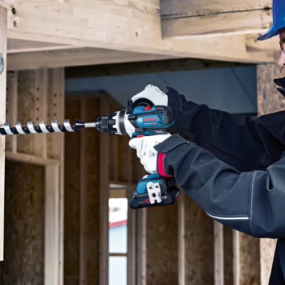 Homem com capacete usando furadeira sem fio para perfurar madeira numa construção