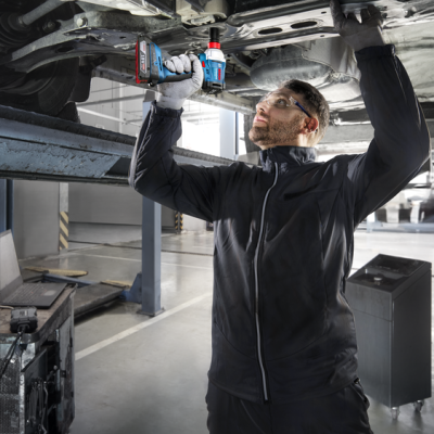 Homem a usar chave de impacto sob carro numa oficina