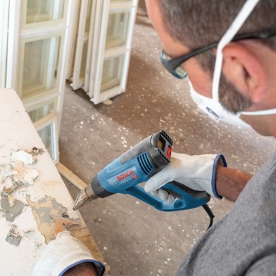 Pessoa a usar pistola de ar quente Bosch para remover tinta de porta branca