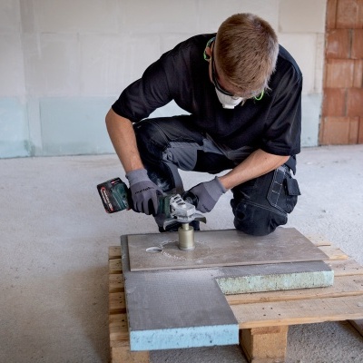 Homem usa ferramenta elétrica para cortar placa cinza em palete