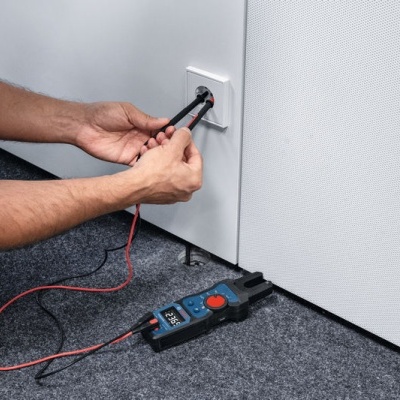 Multímetro digital perto de uma tomada branca com fios