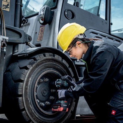 Pessoa com capacete amarelo a trabalhar numa roda de veículo pesado cinzento