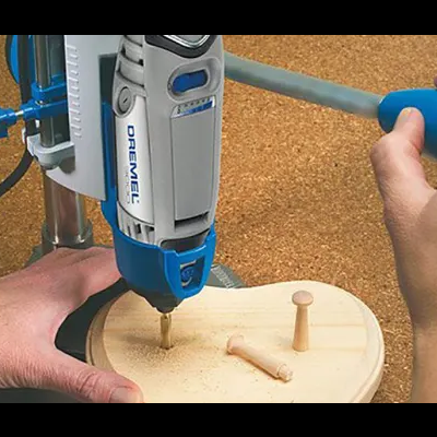 Furadeira Dremel cinza e azul furando chapa de madeira redonda clara