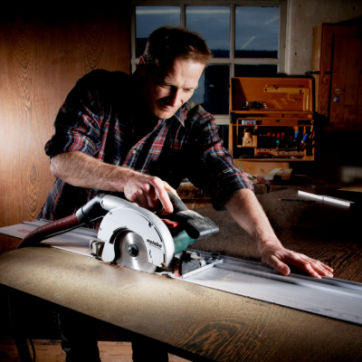 Serra circular elétrica Metabo cinza e preto a cortar tecido castanho numa mesa de madeira numa oficina