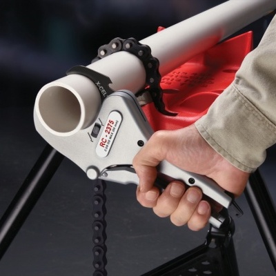 Ferramenta de corte de tubo com corrente em ferro e corpo cinzento a ser usada num tubo branco.