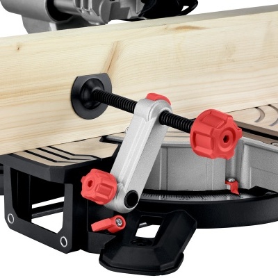 Grampo de fixação preto e vermelho a segurar madeira numa serra de esquadria.