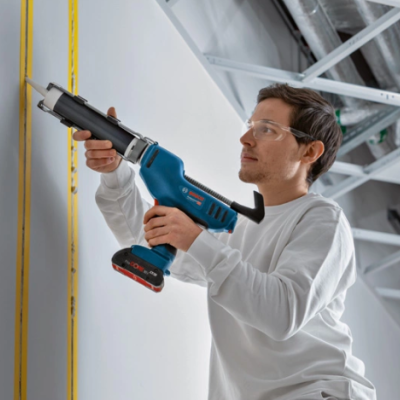 Homem usando pistola de silicone para aplicar selante numa parede branca