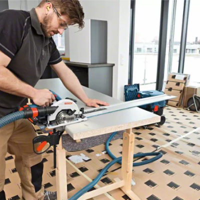 Homem a usar serra circular Bosch em suporte de madeira numa divisão interior com chão protegido