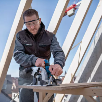 Homem a usar óculos de proteção a cortar madeira com serra circular numa obra ao ar livre