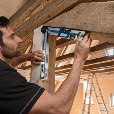 Homem a medir viga de madeira com ferramenta de medição