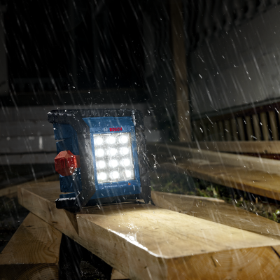 Lanterna de trabalho BOSCH Professional acesa sobre tábuas de madeira na chuva