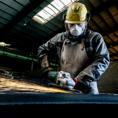 Trabalhador com equipamento de proteção usando rebarbadora numa oficina industrial