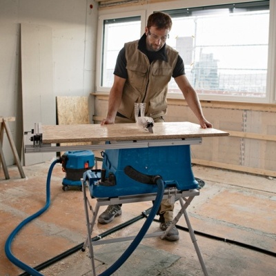 Homem a usar serra circular azul e preta num espaço de trabalho em construção