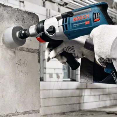 Pessoa usando furadeira elétrica Bosch Professional azul e preta numa parede de cimento cinzenta