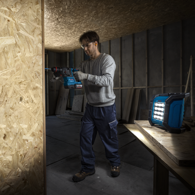 Pessoa a usar uma furadeira elétrica azul Bosch em construção interior com lanterna Bosch.