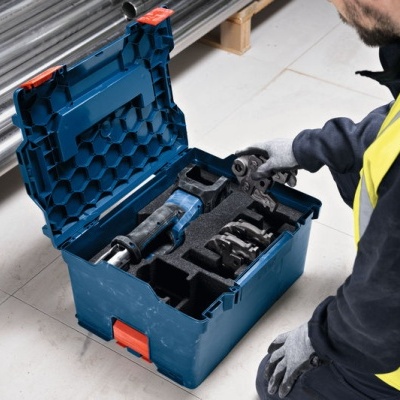 Estojo azul com ferramentas organizadas em espuma preta, homem com colete amarelo manuseando as ferramentas no chão