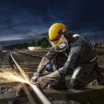 Trabalhador com capacete e máscara a trabalhar num carril ferroviário à noite