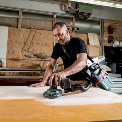 Homem usando lixadora elétrica Bosch numa oficina de carpintaria