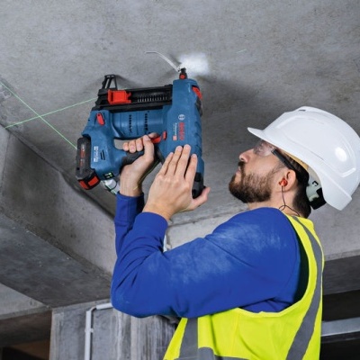 Homem com capacete branco usando berbequim azul numa construção