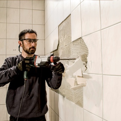 Homem a remover azulejos brancos com ferramenta elétrica