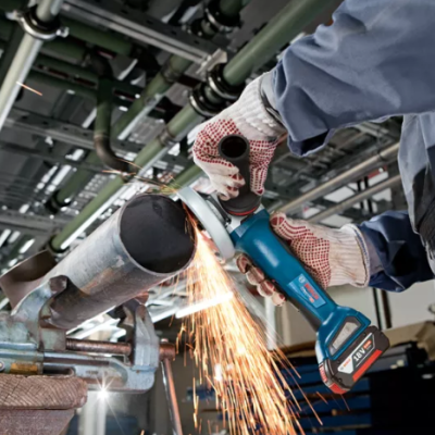 Pessoa a cortar tubo metálico com rebarbadora elétrica azul em ambiente industrial