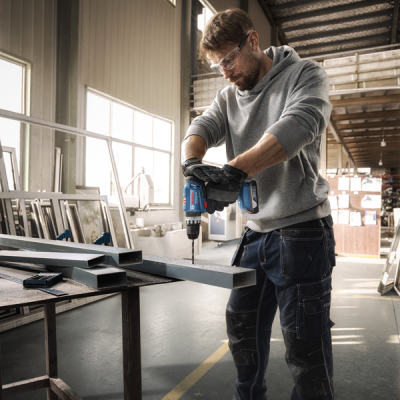 Homem a usar furadeira eléctrica em estrutura metálica dentro de oficina