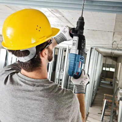 Homem com capacete amarelo usando furadeira para perfurar teto em construção