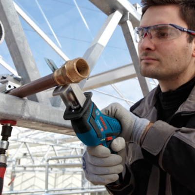 Homem a usar ferramenta elétrica para cortar tubo de metal num ambiente industrial