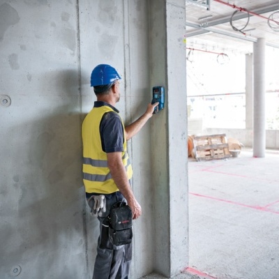 Trabalhador de construção com colete e capacete a usar aparelho na parede em obra