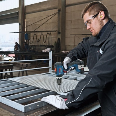 Pessoa a usar furadeira eléctrica numa estrutura metálica numa oficina