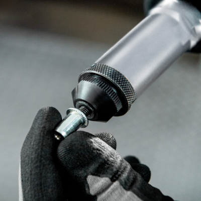 Ferramenta elétrica metálica e mão com luva segurando peça pequena