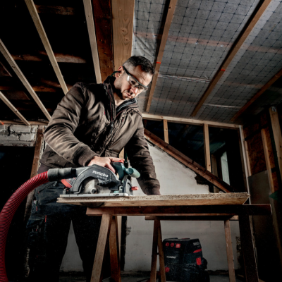 Homem a cortar madeira com serra circular numa bancada em espaço interior em construção