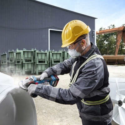 Homem com equipamento de segurança esmerilhando uma superfície metálica branca ao ar livre