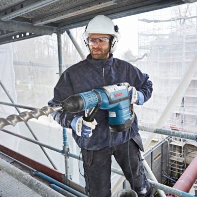 Trabalhador de construção usando berbequim elétrico Bosch em parede de betão num andaime