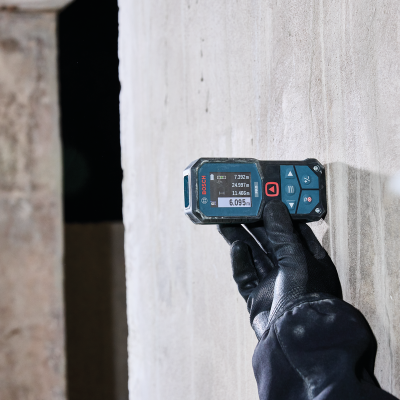 Dispositivo medidor a laser BOSCH PRO segurado contra parede cinza.