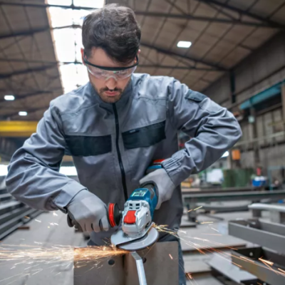 Homem a usar esmerilhadora azul num metal dentro de uma oficina