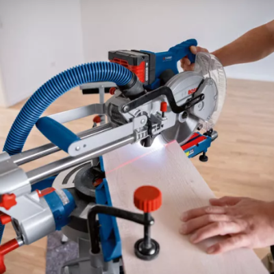 Máquina de cortar madeira elétrica com estrutura azul e peças vermelhas em uso