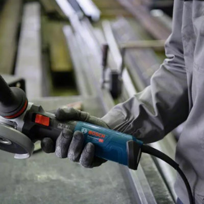 Esmerilhadora Bosch azul e preta numa mão com luvas, num ambiente industrial