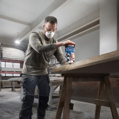 Homem a usar lixadora elétrica numa mesa de madeira numa oficina