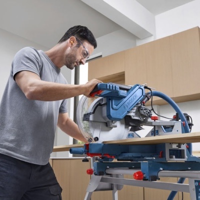 Homem a usar serra de esquadria elétrica para cortar madeira no interior de uma sala