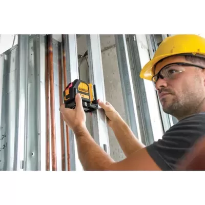 Homem com capacete e óculos segurando nível laser DEWALT junto a estrutura metálica e tubos
