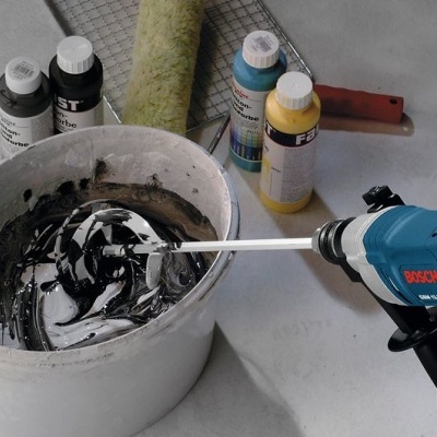 Furadeira Bosch azul com haste misturadora em balde de tinta preta, tintas coloridas e pincel