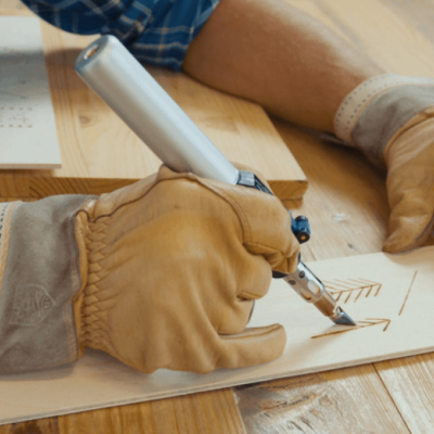 Pessoa com luvas a desenhar casa numa tábua de madeira