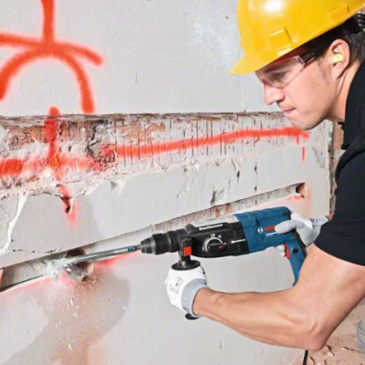 Homem com capacete amarelo a cortar parede com ferramenta elétrica