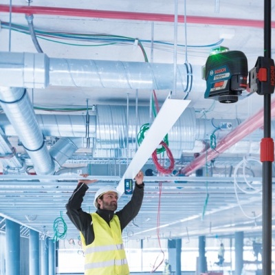 Trabalhador com colete refletor usando nível laser Bosch verde em construção industrial
