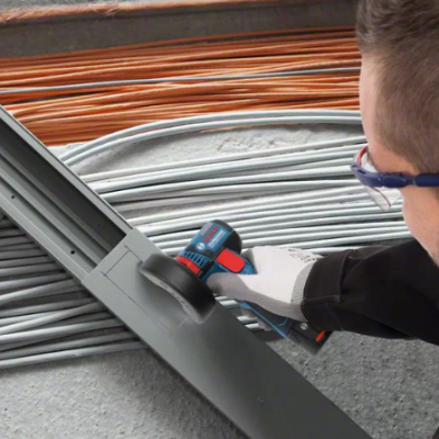 Homem a usar ferramenta elétrica para aparafusar estrutura metálica com cabos ao fundo