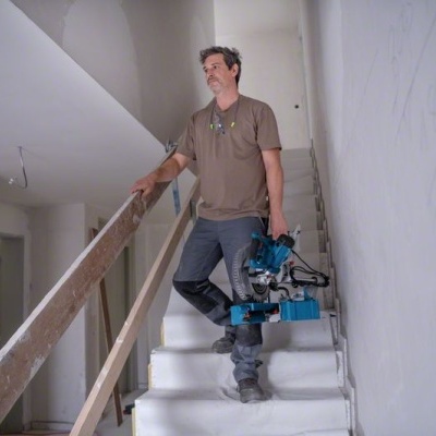 Homem a subir escadas interiores com serra elétrica azul nas mãos