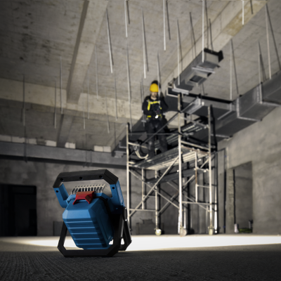 Lanterna portátil azul com detalhes pretos no chão de obra com trabalhador ao fundo