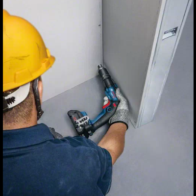 Trabalhador com capacete e luvas a usar furadeira azul num canto interior