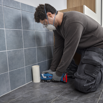 Homem a usar ferramenta elétrica Bosch junto a azulejos cinzentos e tubo branco
